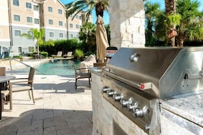 An outdoor pool area with a grill and lounge chairs.