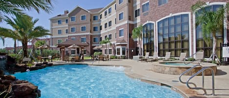 A hotel with a swimming pool, lounge chairs, and palm trees.