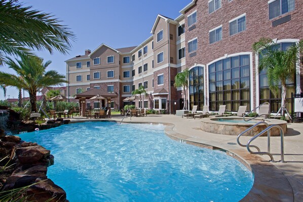 A hotel with a swimming pool, lounge chairs, and palm trees.