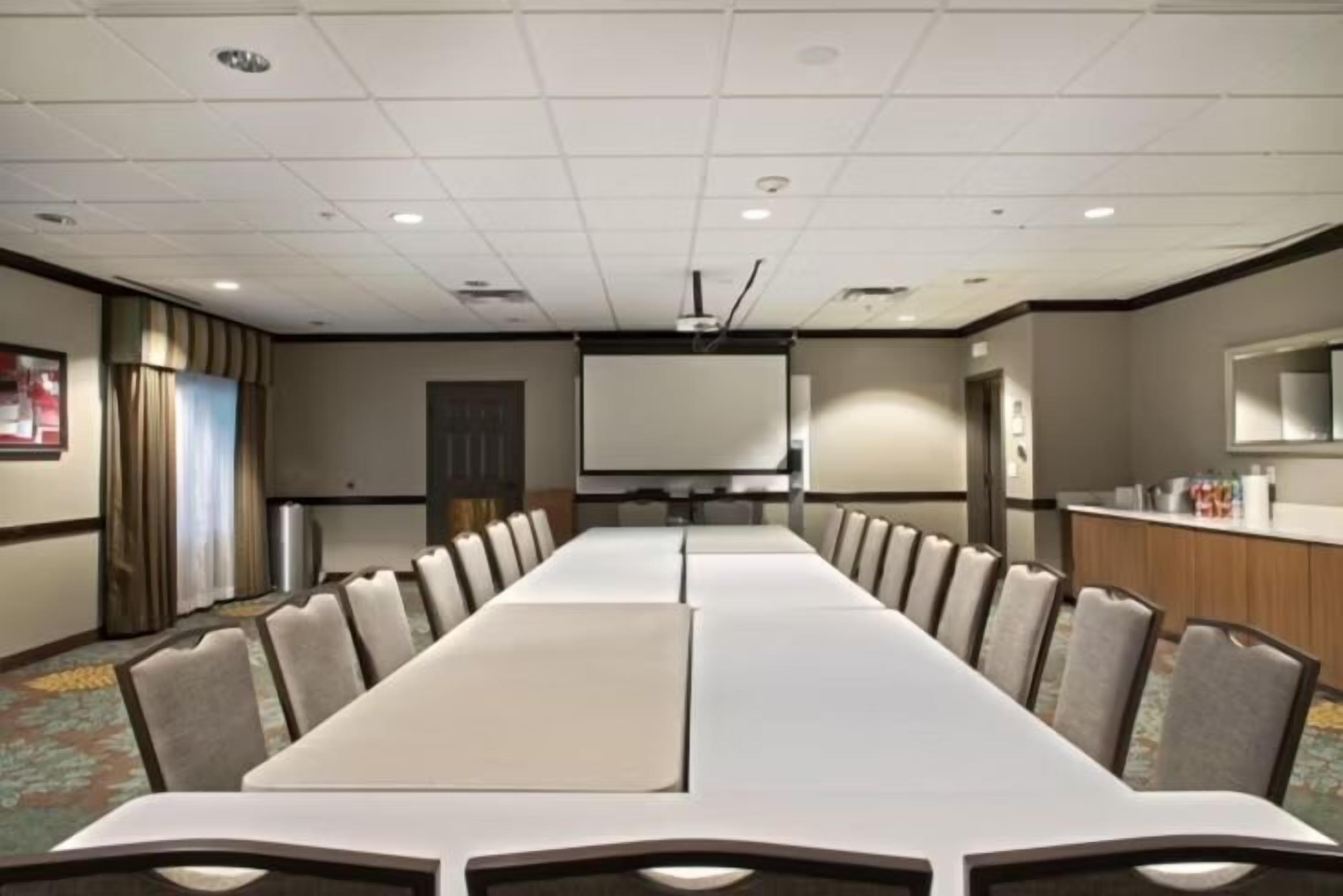 A conference room with a long table, chairs, a projector screen, and a whiteboard.