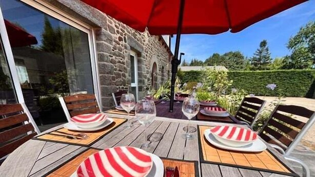 Un área de comedor al aire libre con pared de piedra, mesa de madera y sombrillas rojas.