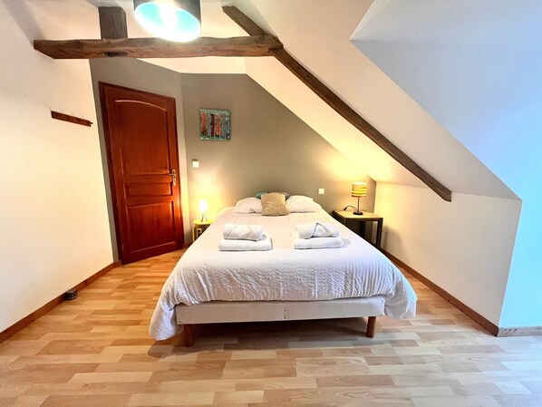 A bedroom with a bed, wooden floor, a door, a painting, and a lamp.