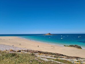 A beach with clear skies, calm waters, and a rocky outcrop in the foreground.