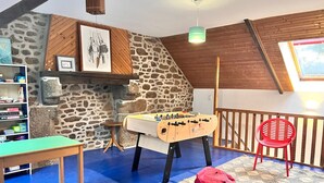 Una habitación acogedora con una mesa de fútbol de mesa, una silla roja, una estantería y una pared de piedra.