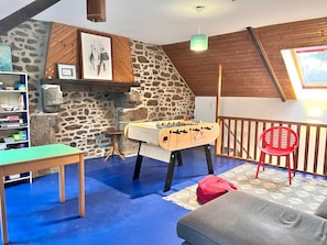 A cozy room with a foosball table, a red chair, a bookshelf, and a stone wall.