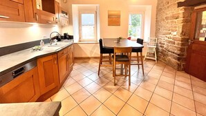Una cocina con armarios de madera, una mesa de comedor con sillas, un ventanal y una pared de piedra.