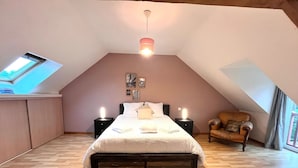 Un dormitorio con techo inclinado, una cama con cubrecama blanco, dos lámparas de noche, una silla de madera y un tragaluz.