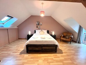 A bedroom with a sloped ceiling, a bed with a white bedspread, two bedside lamps, a wooden chair, and a skylight.