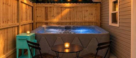 A hot tub with a table and chairs, surrounded by a wooden fence, under string lights.