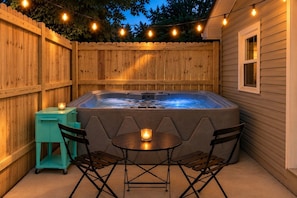 A hot tub with a table and chairs, surrounded by a wooden fence, under string lights. - Bluebird Cabin: The Scenic Hills Cottages (Logan)