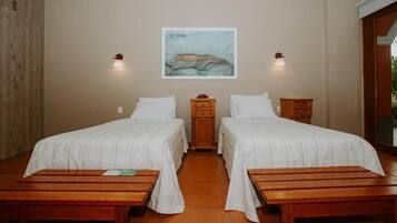 Een kamer met twee bedden, een houten bankje, een klein kastje en een aan de muur hangend schilderij.