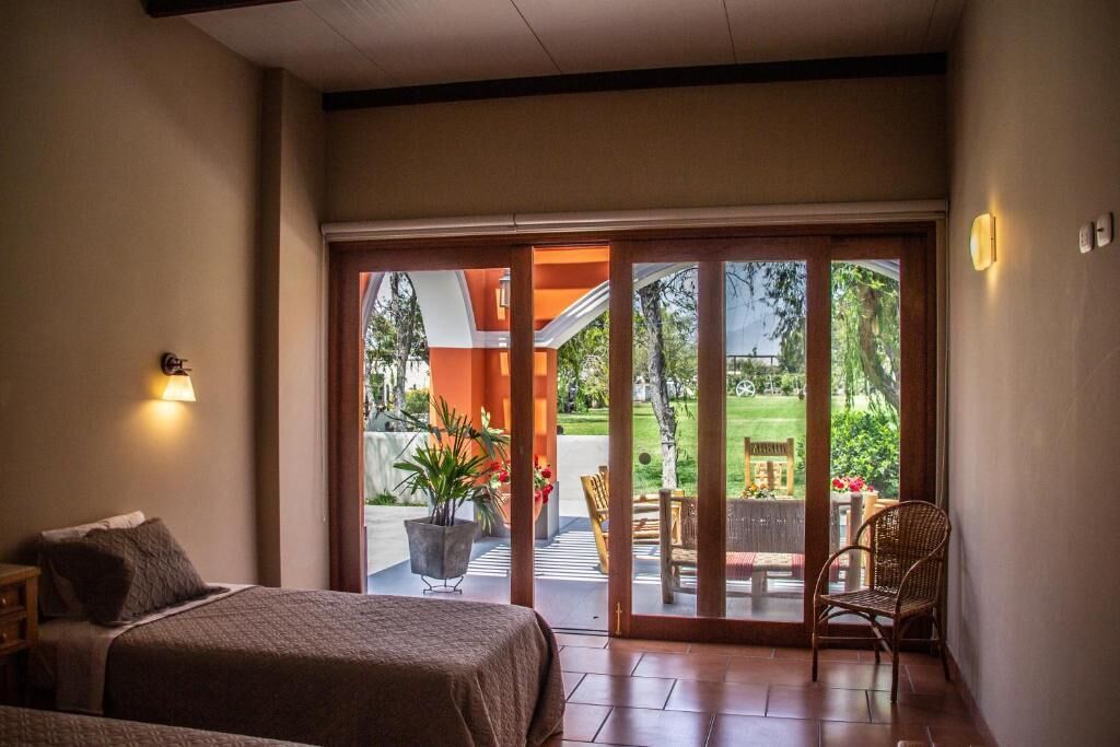 Quarto de hotel com uma cama, uma cadeira e vista da área externa através de uma porta deslizante.