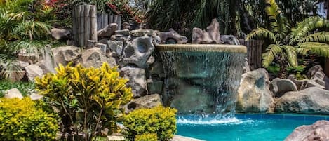 A pool surrounded by rocks and tropical plants.