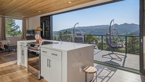 Eine moderne Küche mit einer großen Kochinsel, einem Essbereich mit Tisch und Stühlen sowie ein Balkon mit Bergblick.