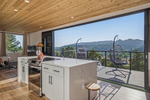 Eine moderne Küche mit einer großen Kochinsel, einem Essbereich mit Tisch und Stühlen sowie ein Balkon mit Bergblick.