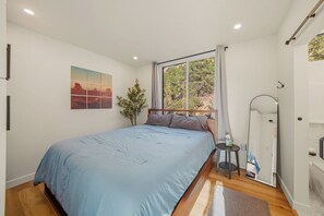 Une chambre à coucher avec un lit, une fenêtre donnant sur un beau paysage, une table de chevet et un miroir.