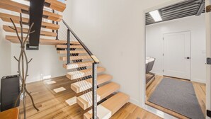 Eine moderne Treppe mit Holzstufen und Metallgeländern, die zu einem Raum mit einer weißen Tür und einem grauen Teppich führt.