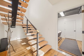 Eine moderne Treppe mit Holzstufen und Metallgeländern, die zu einem Raum mit einer weißen Tür und einem grauen Teppich führt.
