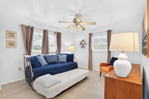 A bedroom with a bed, a desk, a chair, a ceiling fan, and a window with curtains. - Aloha Cottage at Sapphire Shores (Sarasota)