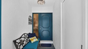 Un couloir avec une porte bleue, un banc doté d’un coussin et un tapis à motifs.