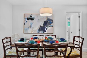 Comedor con mesa dispuesta para cuatro personas, rodeada de sillas de madera con cojines estampados.