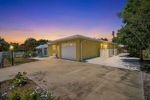 A single-story building with a garage, surrounded by a gravel driveway and a small garden area. - Aloha Cottage at Sapphire Shores (Sarasota)
