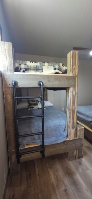 Una cama litera con escalera, cabecera de madera y una colcha a cuadros.