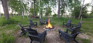 A campfire surrounded by black Adirondack chairs in a forest setting. - Lakseside Lookout 3-bedroom cabin on Leech Lake (Walker)