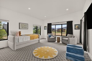 Ein modernes Schlafzimmer mit einem Bett, zwei Sesseln, einem kleinen Tisch und einem großen Fenster mit Blick ins Freie.