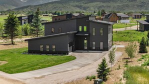 Ein modernes, zweistöckiges Haus mit Auffahrt und Blick auf Berge im Hintergrund.