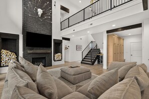 Uma sala de estar ampla com lareira, uma escada que leva a um andar superior e um grande armário de madeira.