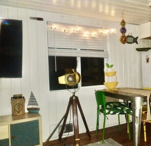 A room with a tripod-mounted camera, a dining table with chairs, and a window with blinds.