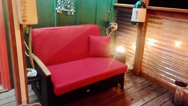 A red sofa in a room with green walls, a wooden floor, and a window with blinds. - Peaceful 1-bedroom cabin in adorable Moclips perfect for relaxing (Moclips)