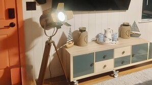 A room with a mounted flat-screen TV, a tripod with a light, and a wooden cabinet with drawers. - Peaceful 1-bedroom cabin in adorable Moclips perfect for relaxing (Moclips)