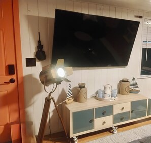 Ein Zimmer mit einem an der Wand befestigten Flachbildfernseher, einem Stativ mit Lampe und einer Holzkabine mit Schubladen.