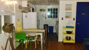A compact kitchen with a dining area, a blue door, and a shelf with kitchenware. - Peaceful 1-bedroom cabin in adorable Moclips perfect for relaxing (Moclips)