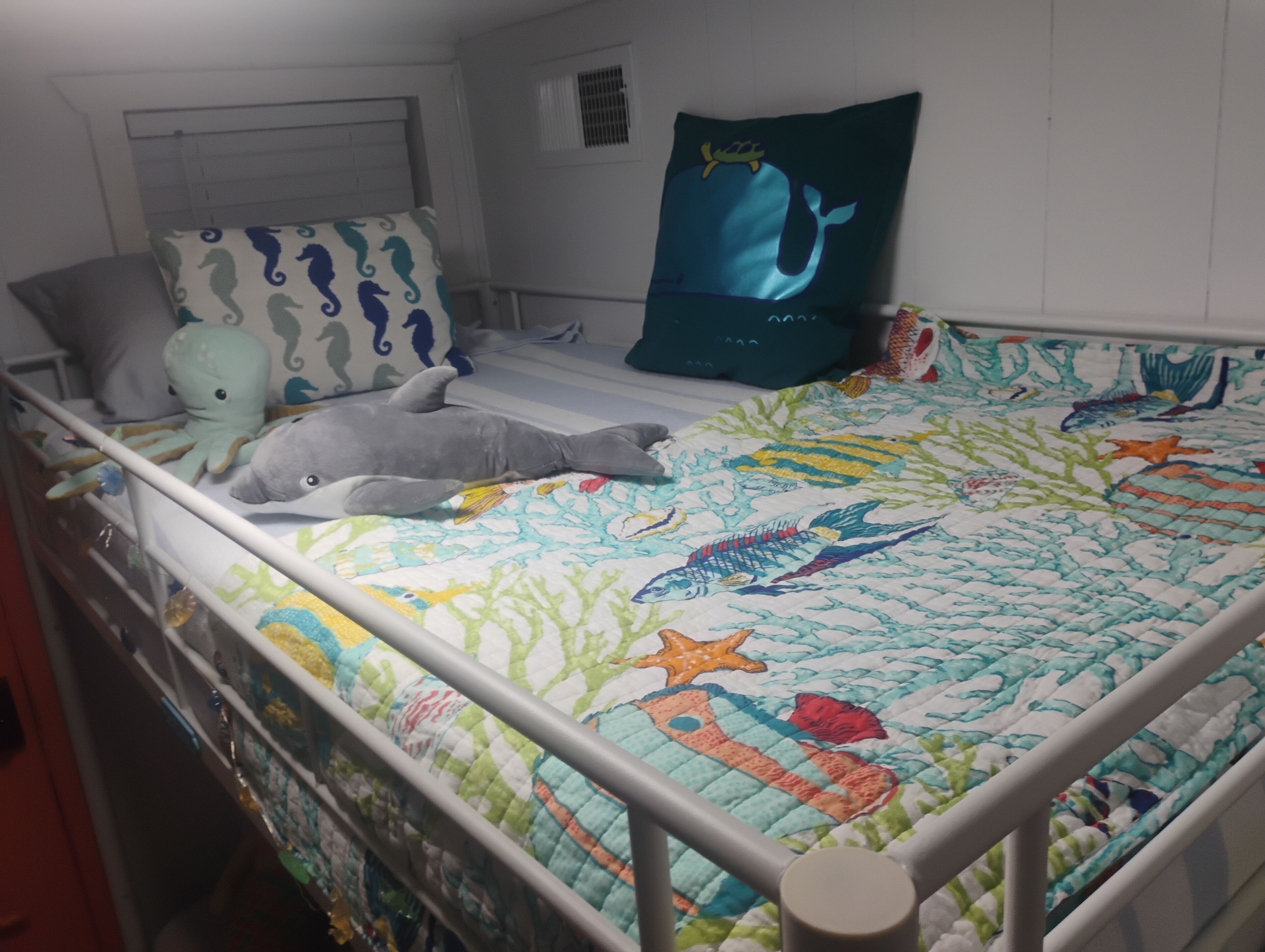 A child's bed with a colorful quilt, a whale pillow, and a dolphin plush toy.