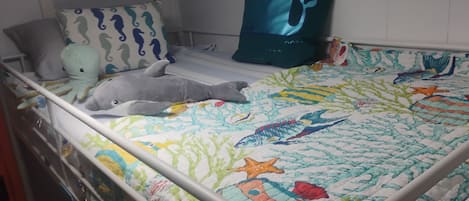 A child's bed with a colorful quilt, a whale pillow, and a dolphin plush toy.