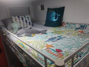 Ein Kinderbett mit einer farbenfrohen Decke, einem Wal-Kissen und einem Delfin-Plüschtier.
