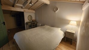 Ein Schlafzimmer mit einem großen Bett, einem Nachttisch mit Lampe, einer Kommode und einer herzförmigen Dekoration an der Wand.