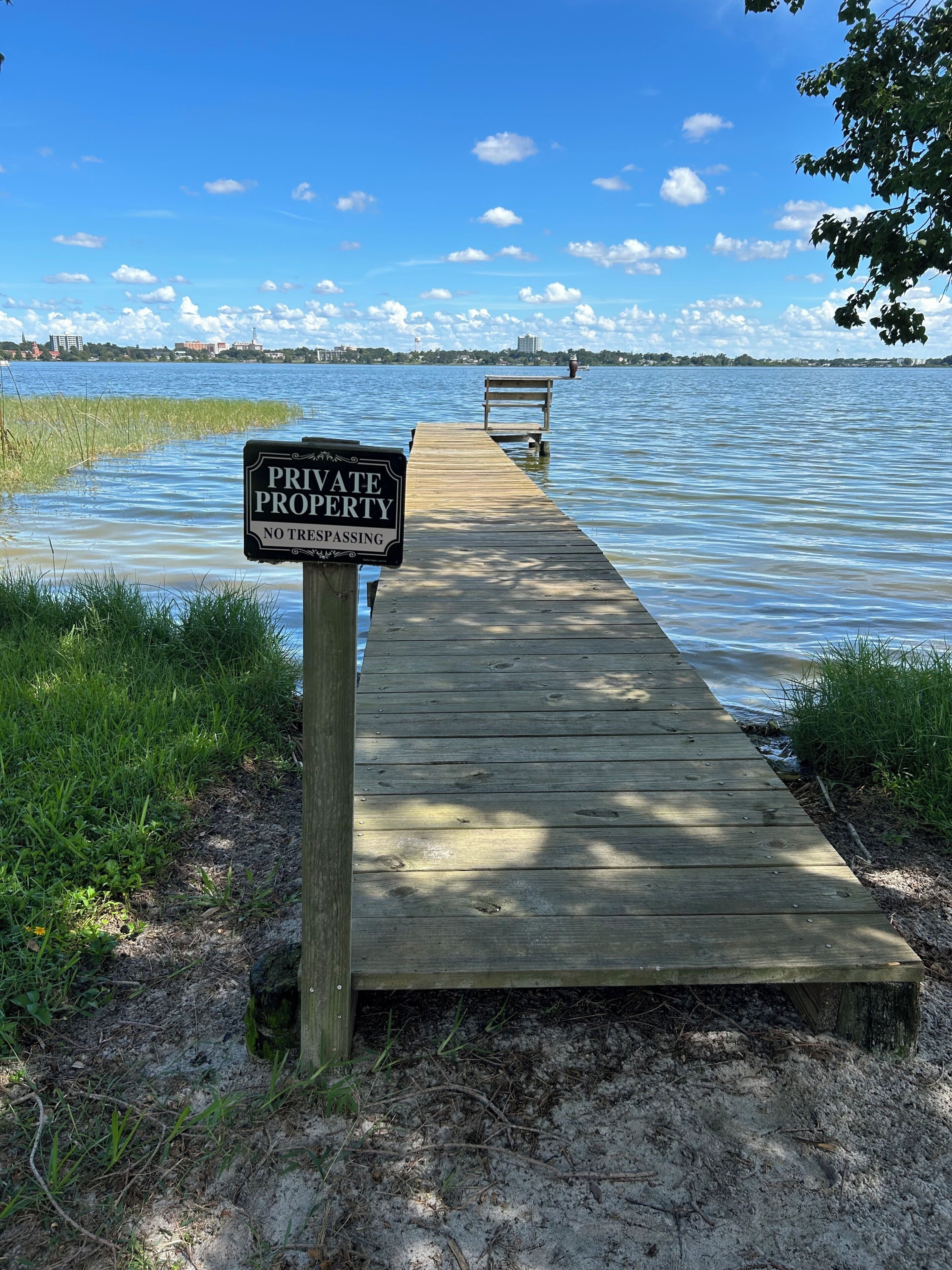 Un muelle de madera que se adentra en un cuerpo de agua, con un letrero al final que indica 'PROPIEDAD PRIVADA, PROHIBIDO EL PASO'.
