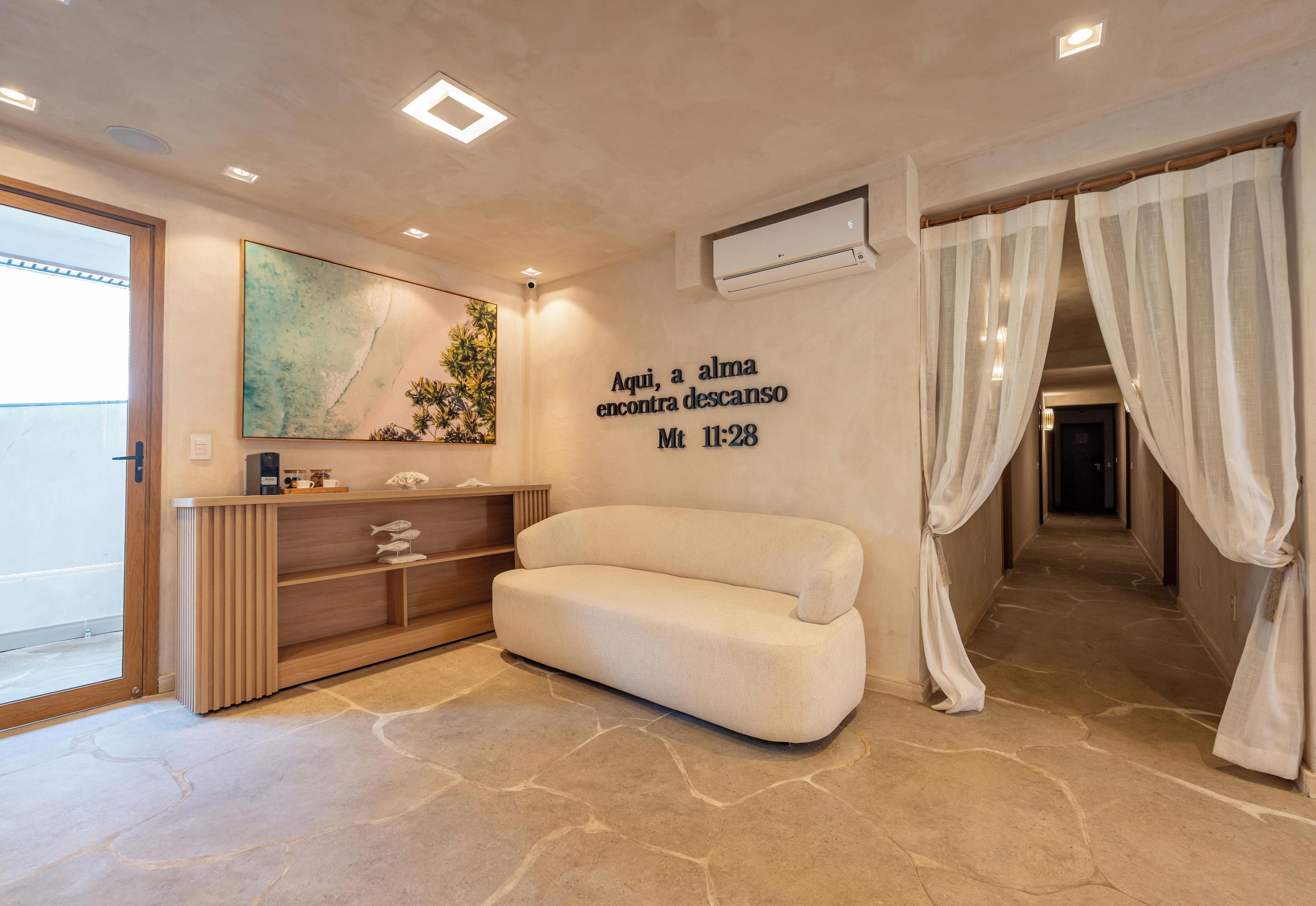 A modern hotel room with a sofa, a wall-mounted artwork, a shelf with decorative items, and a text wall.