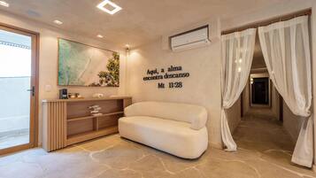 A modern hotel room with a sofa, a wall-mounted artwork, a shelf with decorative items, and a text wall.