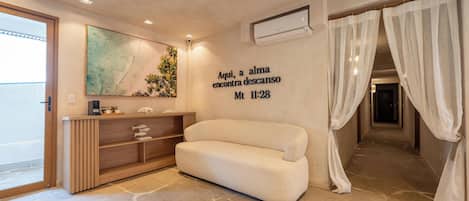 A modern hotel room with a sofa, a wall-mounted artwork, a shelf with decorative items, and a text wall.