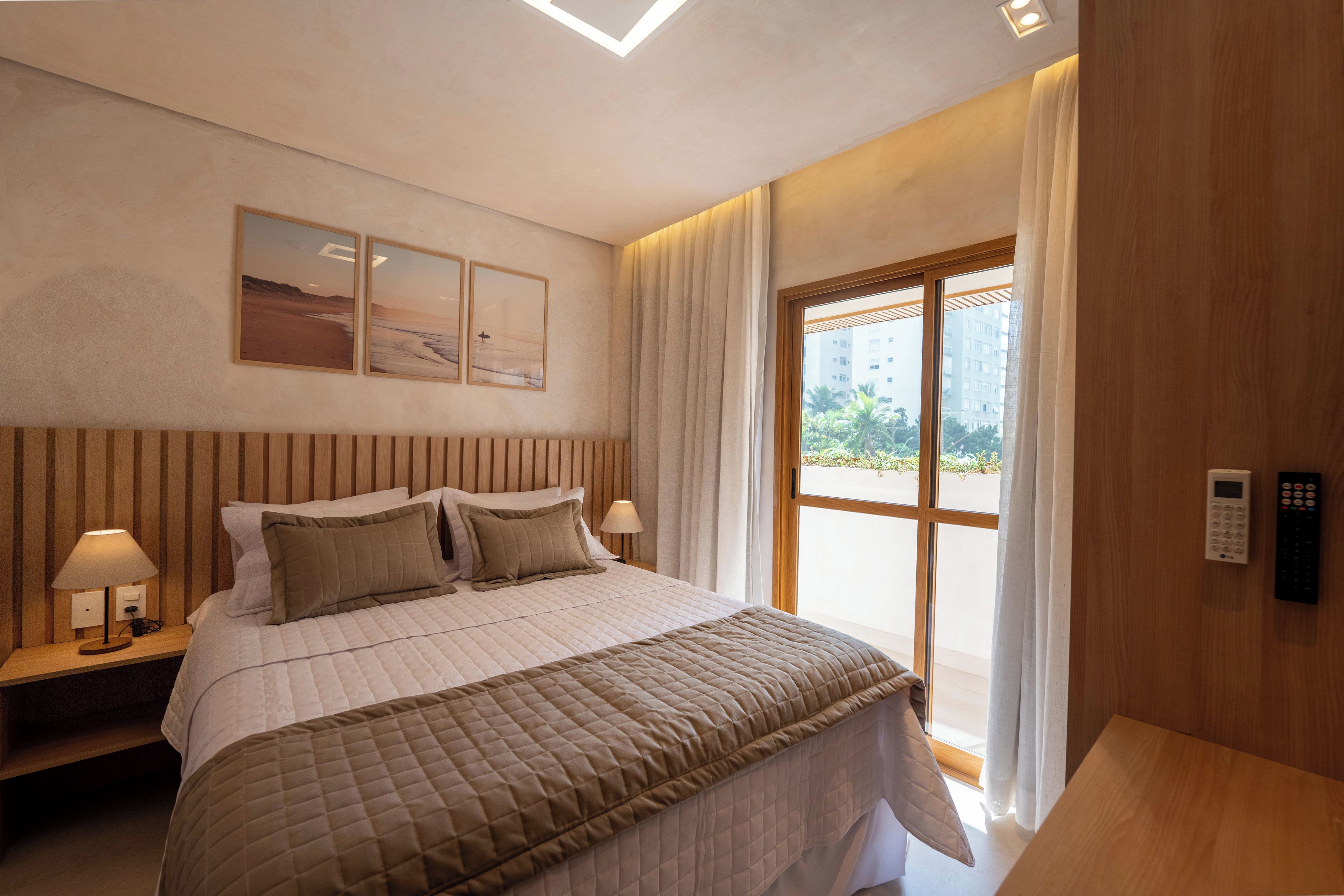 A hotel room with a bed, two bedside tables, a window with curtains, and artwork on the wall.