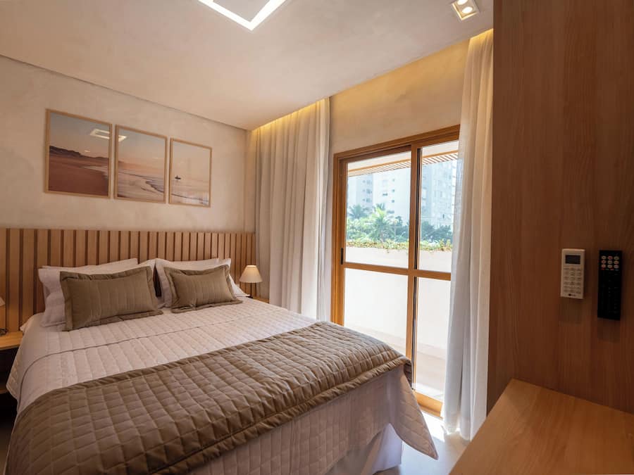 Una habitación de hotel con una cama, dos mesitas de noche, un ventanal con cortinas y una obra de arte en la pared.