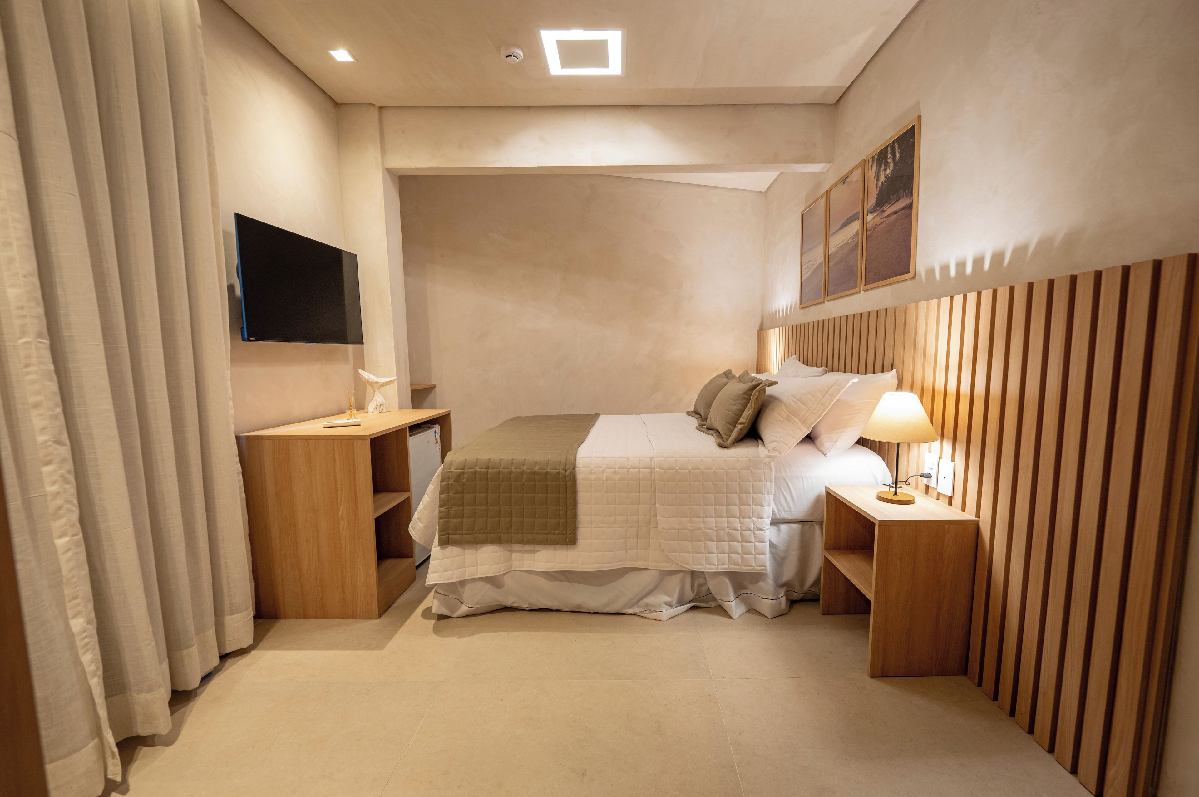 Un dormitorio con cama, mesitas de noche, televisor de pantalla plana, lámpara y ventana con cortinas.