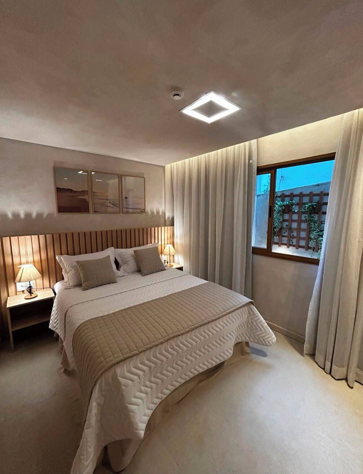 A modern bedroom with a large bed, a nightstand with a lamp, a ceiling light, and a window with curtains.