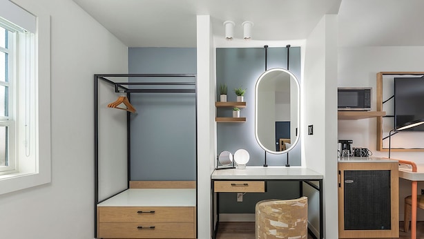 A compact bedroom with a bed, bedside table, mirror, and a small seating area.