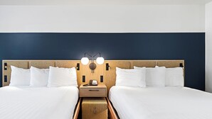A hotel room with two beds, a nightstand with a lamp, and a small table.